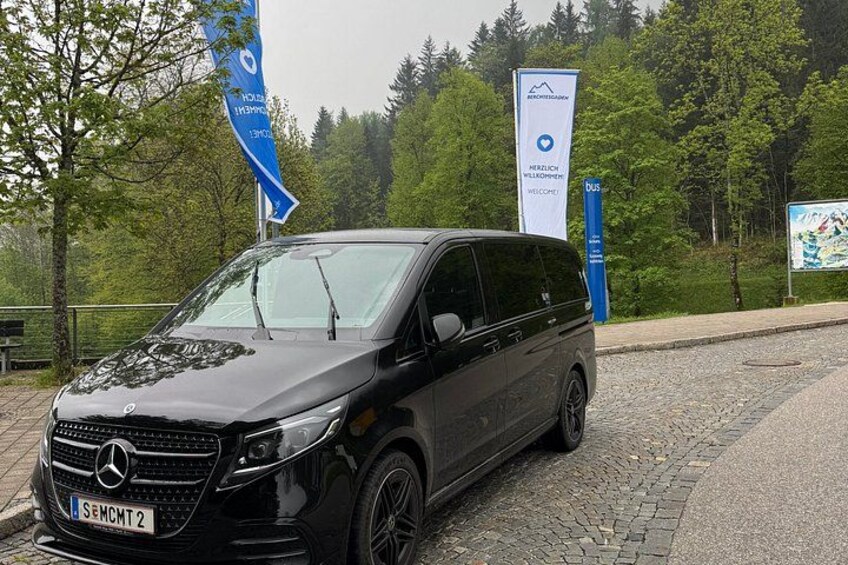 A black Mercedes-Benz Sprinter van parked on a cobblestone path with trees and a blue sign in the background. 5