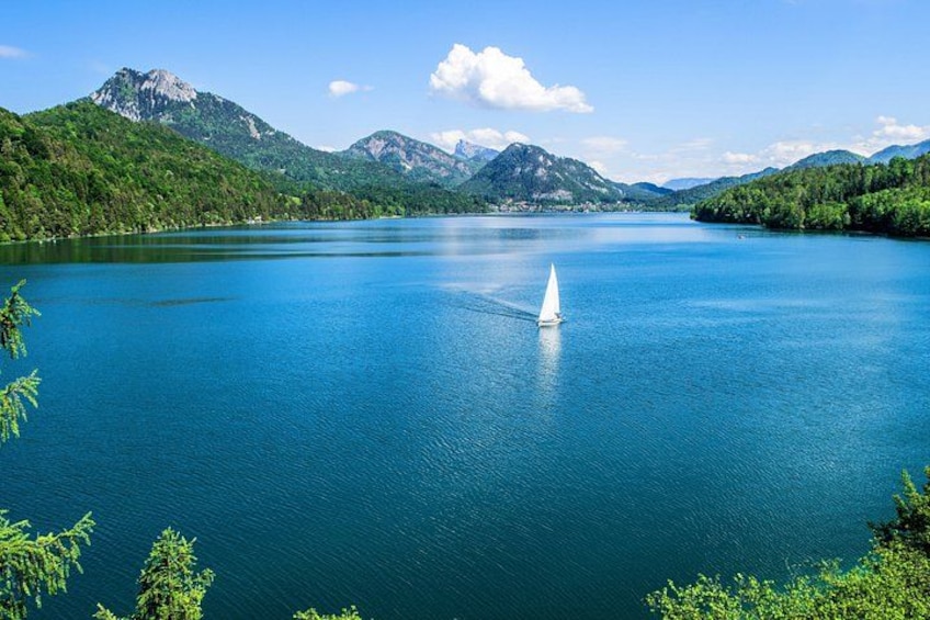 A lake with a sailboat, surrounded by mountains and greenery. 5