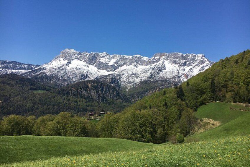 Ein Gebirge mit schneebedeckten Gipfeln, ein grünes Tal mit Bäumen und eine kleine Siedlung. 3