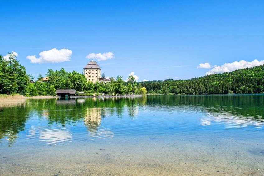 Ein ruhiger See mit klarem Wasser, umgeben von Bäumen und einem Gebäude mit einer Kuppel. 1