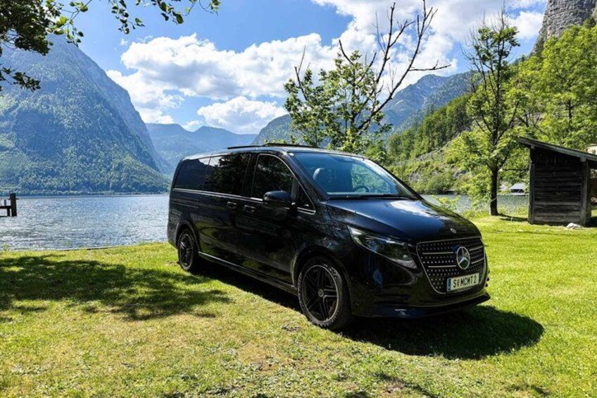 Una furgoneta Mercedes-Benz Sprinter negra estacionada en un césped cerca de un lago con montañas al fondo. 3