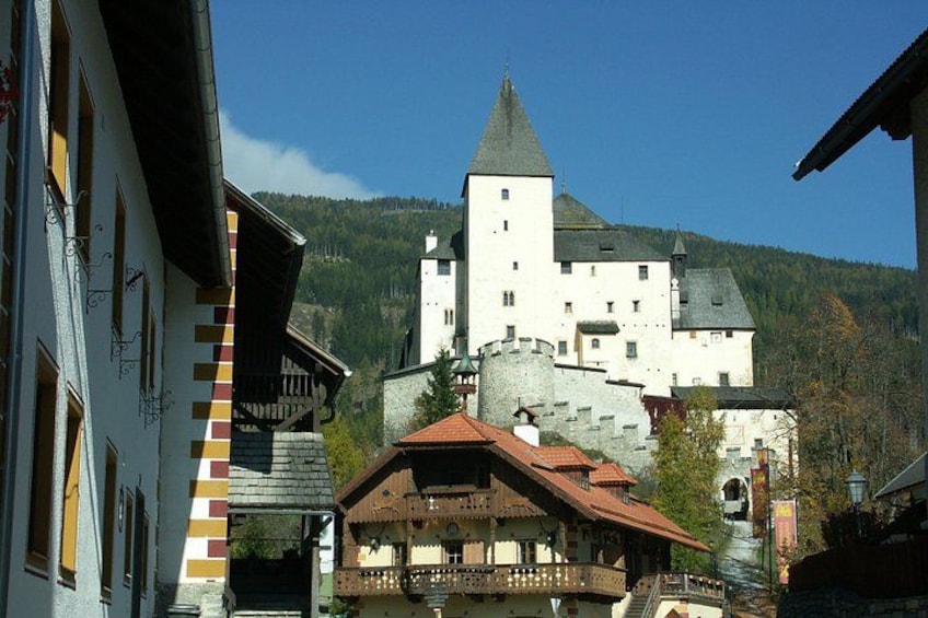 A castle with a tower, surrounded by buildings and a mountainous landscape. 1