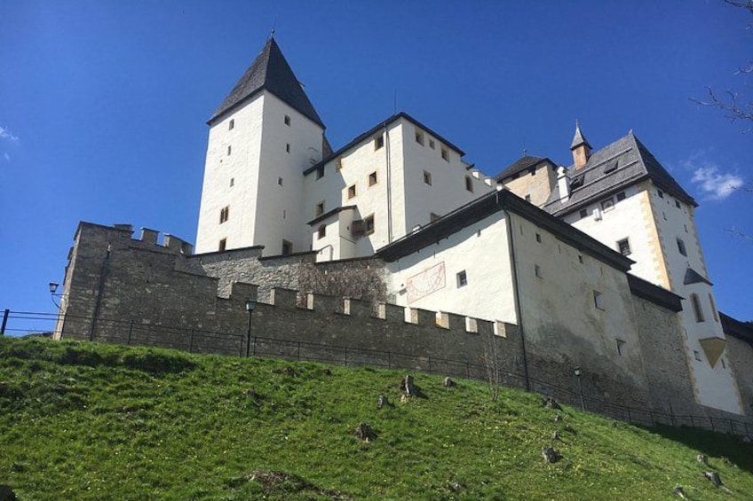Un castillo con varias torres, un muro de piedra y una colina cubierta de césped. 1