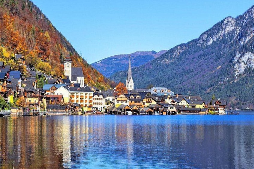 Un pueblo a orillas de un lago, con edificios, una iglesia y montañas al fondo. 1