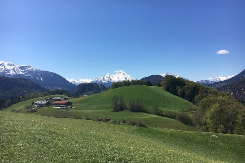 A green valley with a red-roofed building, snow-capped mountains, and a clear blue sky. 3