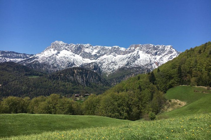 A mountain range with snow-capped peaks, a green valley with trees, and a small settlement. 2