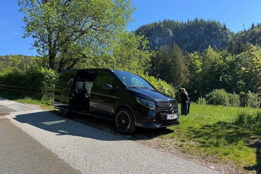 A black van parked on a road with a forested hillside in the background. 1