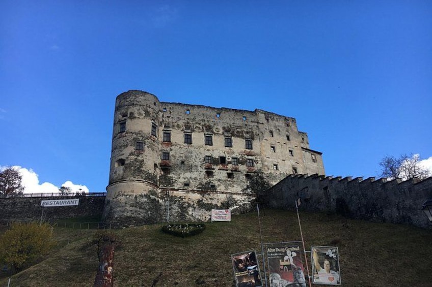 A historic castle with a round tower, a sign for a restaurant, and a small garden area. 4