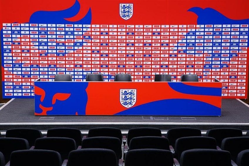 Une table de conférence de presse ornée du logo de la Fédération anglaise de football, entourée de rangées de chaises et surmontée d’un panneau d’affichage portant également le logo de la Fédération anglaise de football. 3