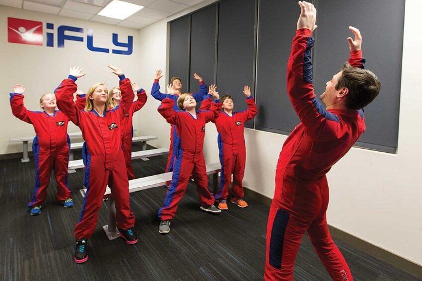 A group of people in red suits performing an exercise in a room with a blackboard and a logo that reads 'iFLY'. 5