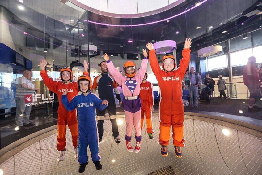 A group of people in a flying suit, indoors, with a glass wall and a sign that reads 'IFLY'. 4