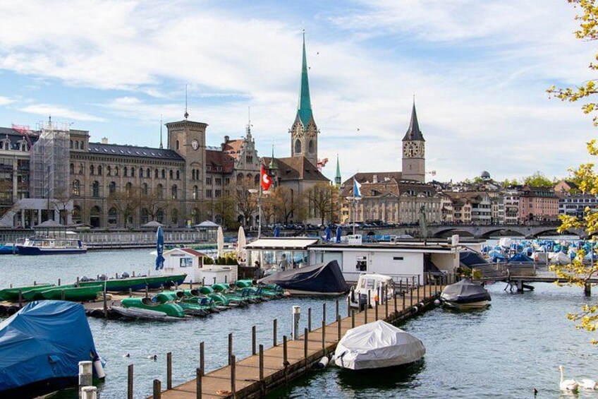 A riverside with boats docked, a bridge, and historic buildings with spires. 2