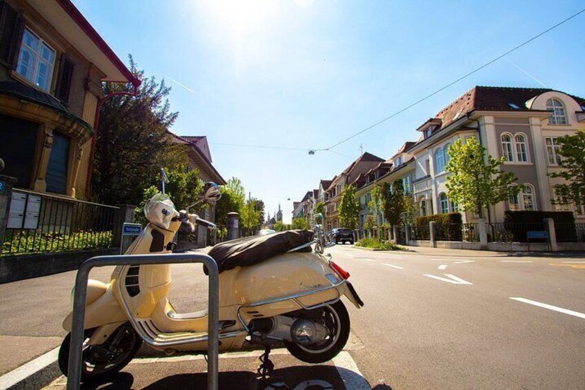 Una scooter estacionada en una calle con edificios y árboles. 4