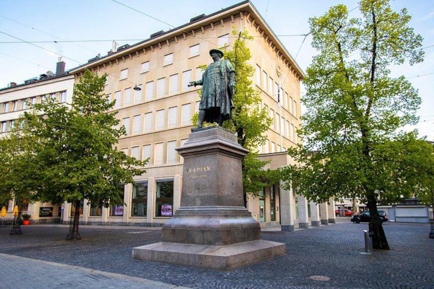 A statue of a man on a pedestal in a square with trees and a building in the background. 2