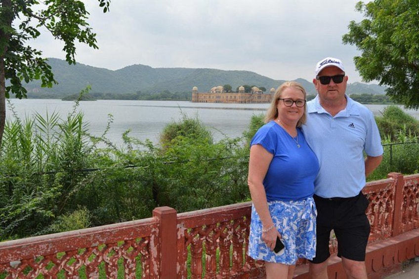 A couple standing on a bridge with a lake and mountains in the background. 3