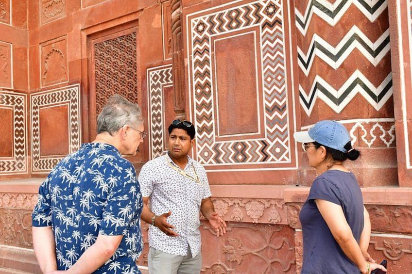 A group of people standing in front of a building with intricate red and white patterned walls. 2