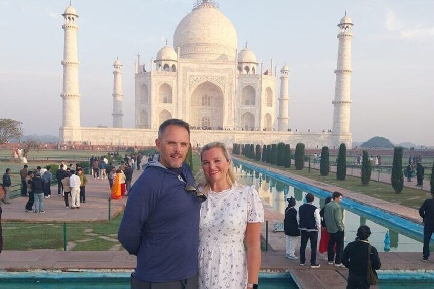 A couple standing in front of the Taj Mahal with a pool and visitors in the background. 4