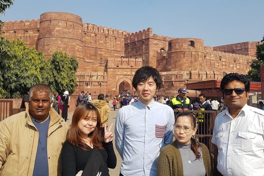 Un gruppo di persone in piedi di fronte a un'imponente fortezza storica, con mura rosse e numerose torri. 4