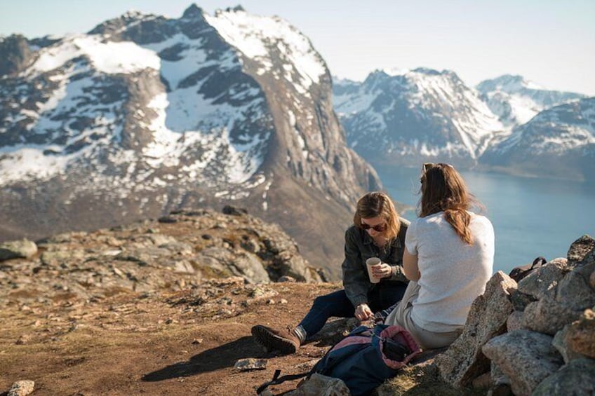 Zwei Personen sitzen auf einem Felsen mit Blick auf eine Berglandschaft und einen See im Hintergrund. 1