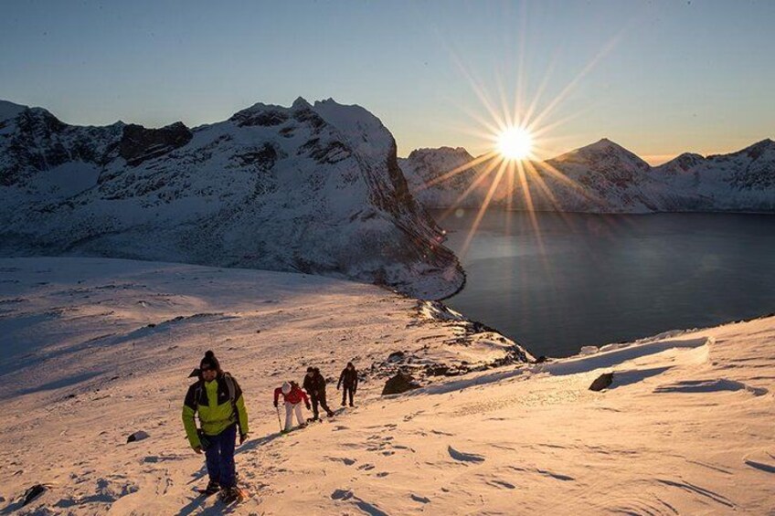 A group of people hiking on a snow-covered path with mountains and a lake in the background. 1