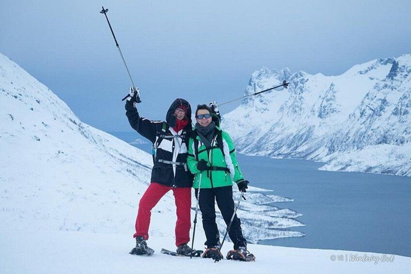 To personer står på ski i et sneklædt bjerg med en sø og flere bjerge i baggrunden. 3