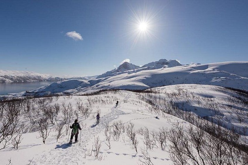 A snowy landscape with a lake, mountains, and people hiking. 2