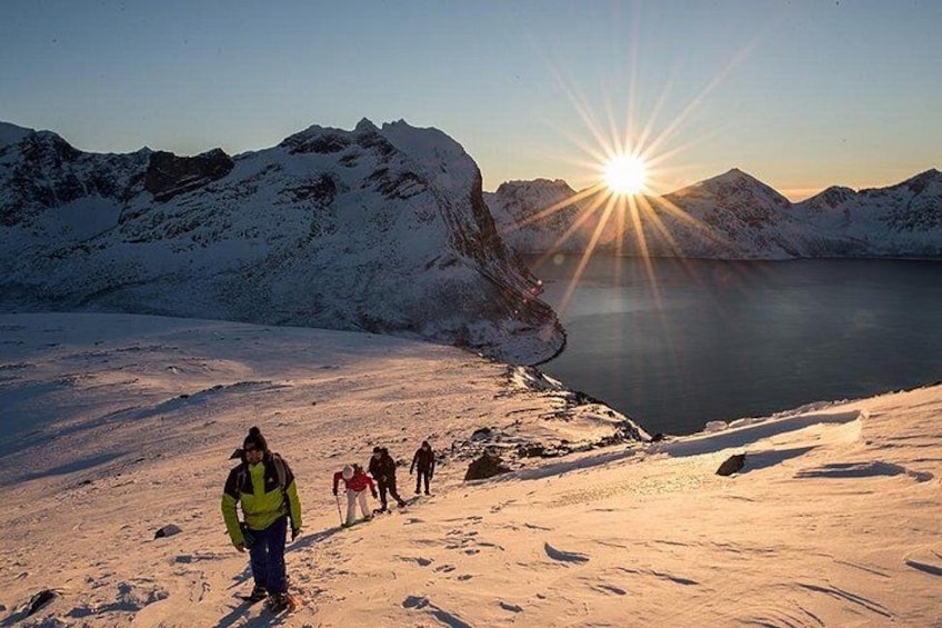 A group of people hiking on a snow-covered trail with a lake and mountains in the background. 1