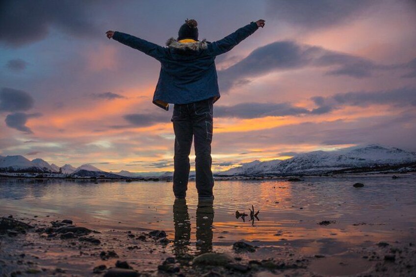 A person standing with arms outstretched on a reflective surface, facing a mountainous landscape during sunset. 4