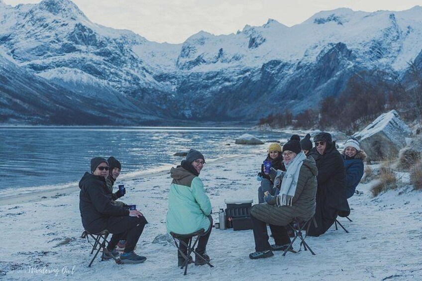 Eine Gruppe von Personen sitzt an Stühlen am Ufer eines verschneiten Sees mit Bergen im Hintergrund. 3