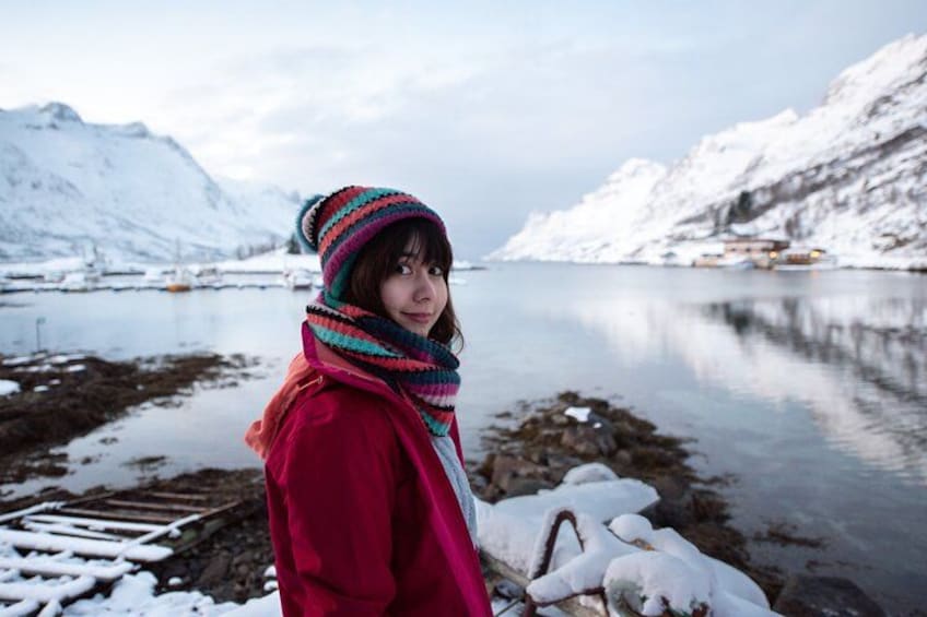 A person standing by a snow-covered lake with mountains in the background. 1