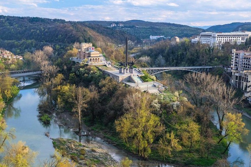 Un río, un puente y edificios rodeados de árboles y colinas. 1