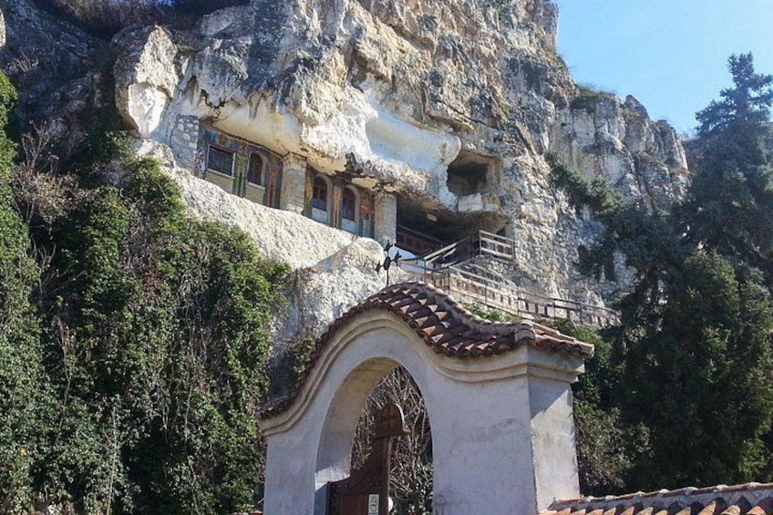Una iglesia excavada en la roca, con fachada de piedra y tejado de tejas, rodeada de vegetación y acantilados rocosos. 3