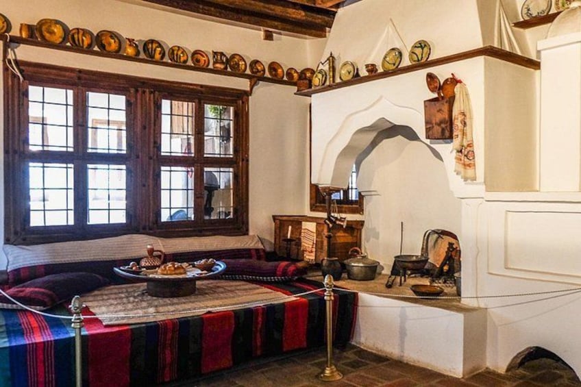 Una habitación tradicional con un banco de madera, un ventanal de múltiples vidrios y una estantería con cerámica. 2