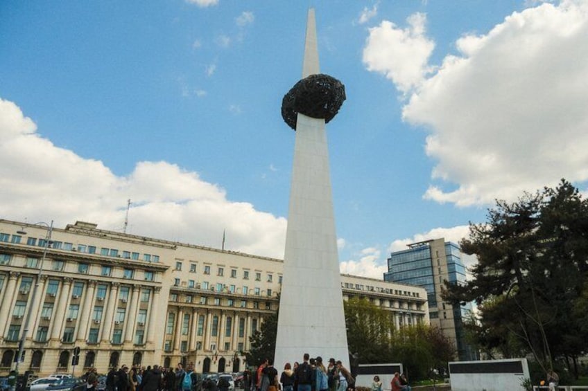 A tall white obelisk with a spherical top, surrounded by a crowd and buildings in the background. 1