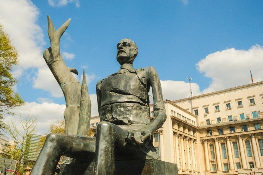 A statue of a seated figure with an outstretched arm, set against a backdrop of a classical building with columns. 5