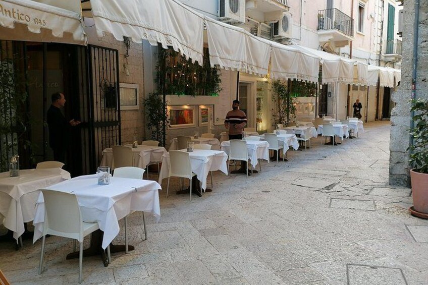 An outdoor café with tables and chairs, a building with a sign, and a person walking. 2