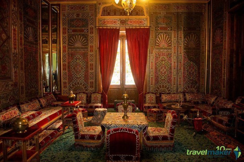 A richly decorated room with intricate patterns, a large window with red curtains, and a chandelier. 4