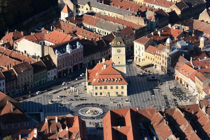 A historic town square with a prominent clock tower, surrounded by traditional buildings with red-tiled roofs. 5