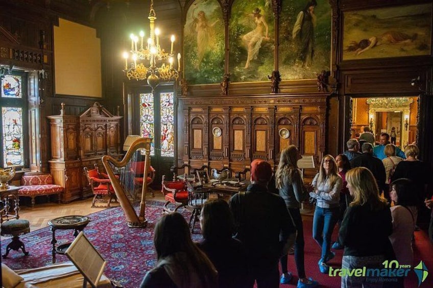 A grand hall with ornate woodwork, a harp, and a group of people gathered. 2
