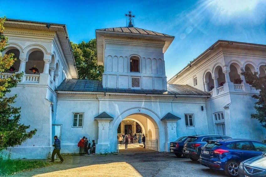 En vit kyrka med ett klocktorn och en välvd ingång. Det finns människor och bilar framför kyrkan. 3