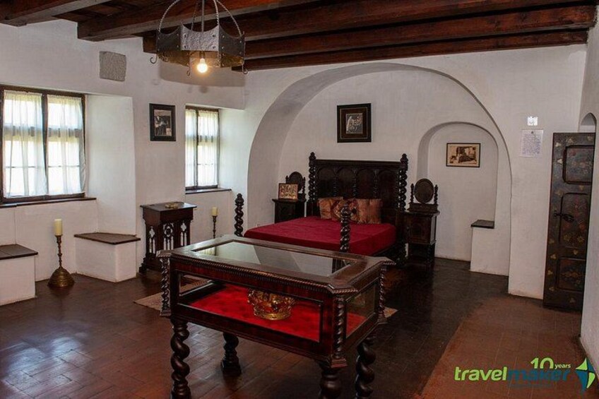 A historical bedroom with a wooden bed, a glass-top table, and a red bedspread. 2