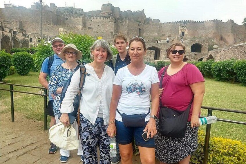 Un groupe de personnes se tient devant un ancien mur de pierre, avec un château en arrière-plan. 4
