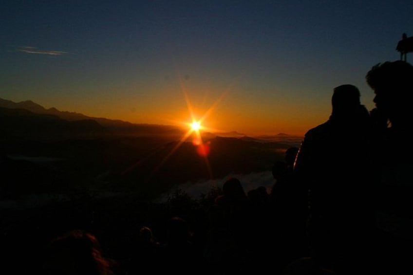 A sunset over a mountainous landscape with silhouettes of people. 3