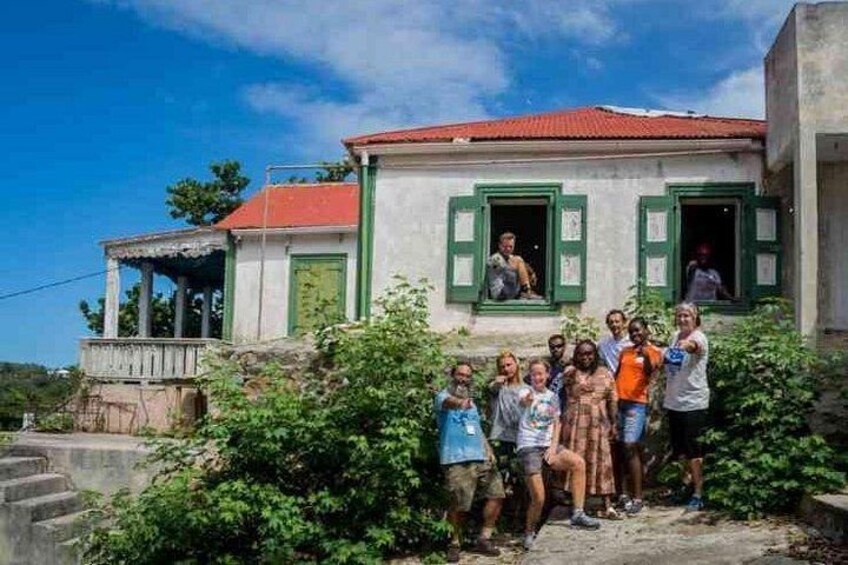 A group of people standing in front of a house with green shutters and a red roof. 2