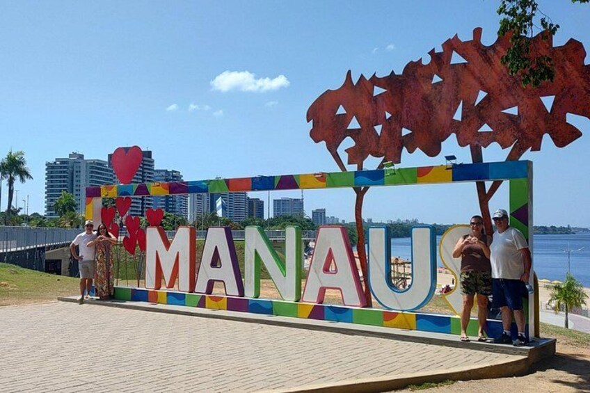 A colorful sign with the word 'MANAU' and a tree sculpture. 1
