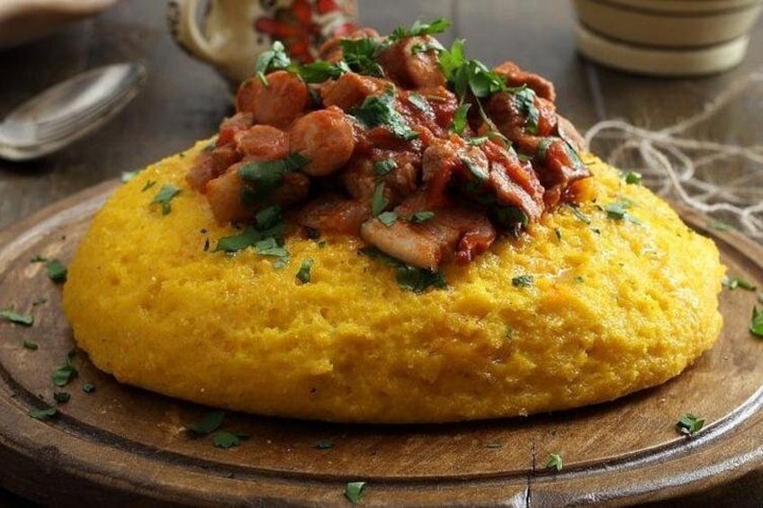 Ein gelber Polenta-Kuchen mit Fleisch-Tomaten-Gemisch, garniert mit Kräutern, auf einem Holzbrett. 3