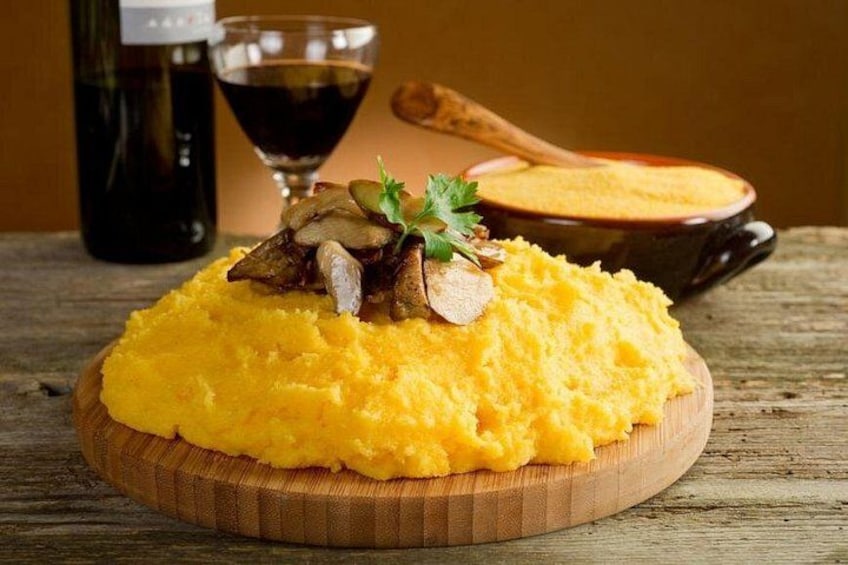 A wooden board with yellow mashed potatoes topped with mushrooms and parsley, a bottle of red wine, and a glass of wine in the background. 1