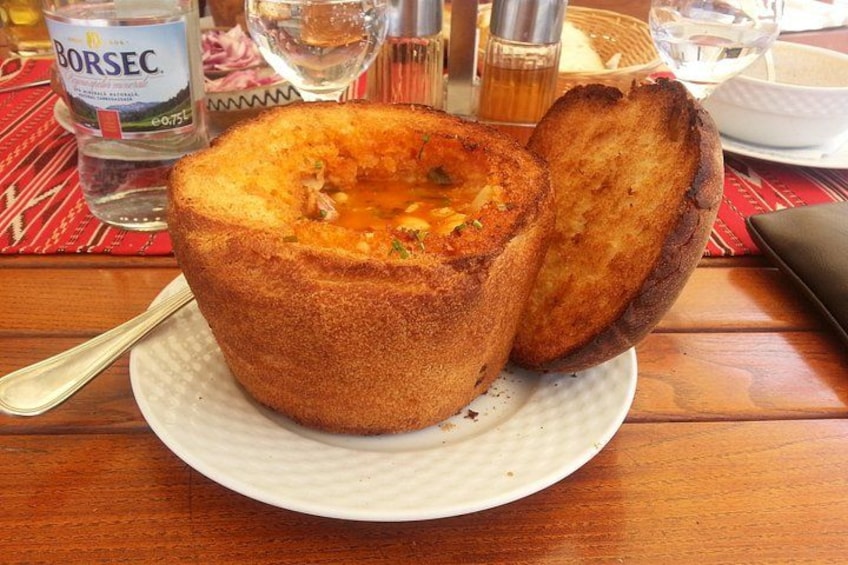 A bread bowl filled with soup, a bottle of Borsec water, and a glass of water on a table. 2