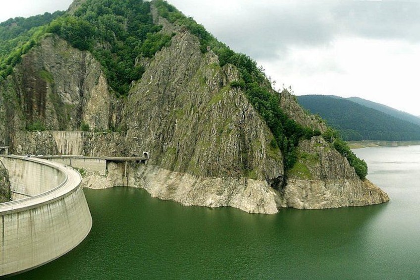A large dam with a curved spillway, surrounded by steep cliffs and a body of water. 3