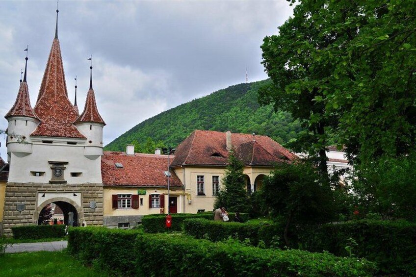 A historic building with a tower, surrounded by lush greenery and a hill in the background. 1